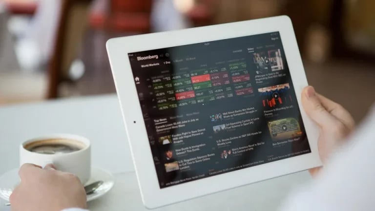 Person viewing stock market data on a tablet beside a cup of coffee.