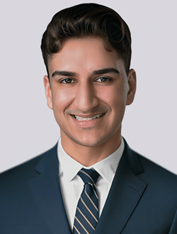 Professional man in suit and tie smiling, posing against gray background for business portrait.
